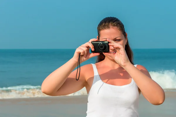 Brunette with a camera taking pictures on the beach — Stock Photo, Image