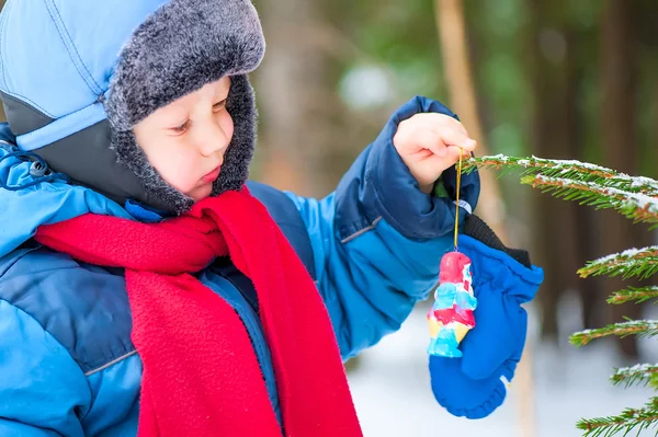 少年は森の中のクリスマス ツリーの装飾にハングアップします。 — ストック写真