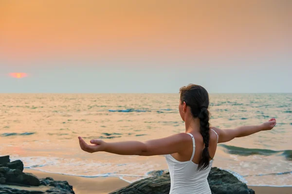 Meisje met zijn handen gespreid bij zonsondergang aan zee — Stockfoto