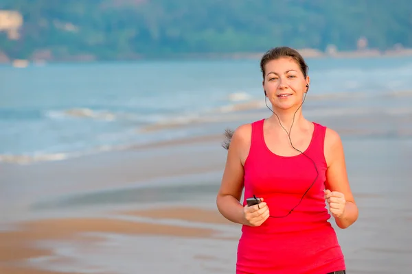 Chica joven corriendo y escuchando música en la playa — Foto de Stock