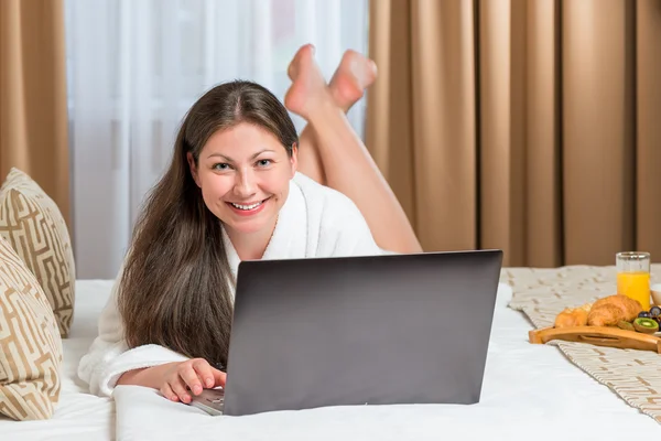 Mooi meisje na de douche liggend op het bed met laptop — Stockfoto
