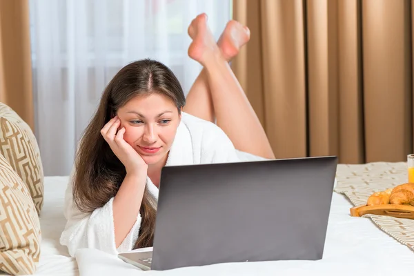 Mujer joven con un ordenador en la cama en el hotel —  Fotos de Stock