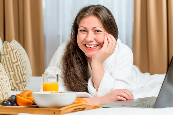 Beautiful and happy girl on the bed with a tray of food — Stockfoto