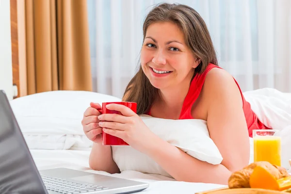 Happy woman with a cup of hot coffee in the morning in bed — Stockfoto