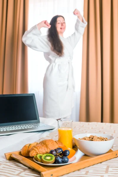 Desayuno en la cama y se estira una mujer en un albornoz — Foto de Stock