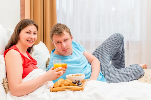 Happy young family eating breakfast in bed — Stock Photo, Image