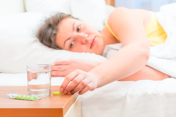 Mujer enferma en la cama buscando pastillas — Foto de Stock