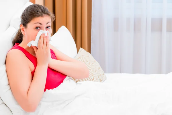 Dívka s rýmou fouká její nos, ležící v posteli — Stock fotografie