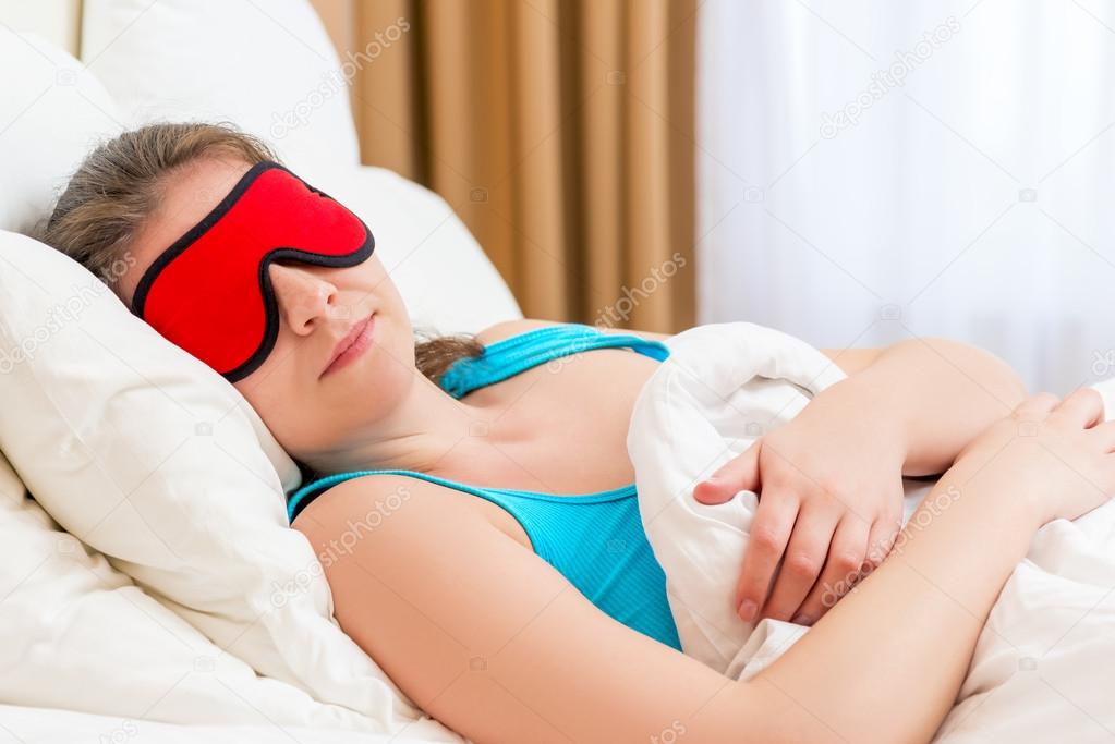 a woman with eye mask sleeping under a blanket