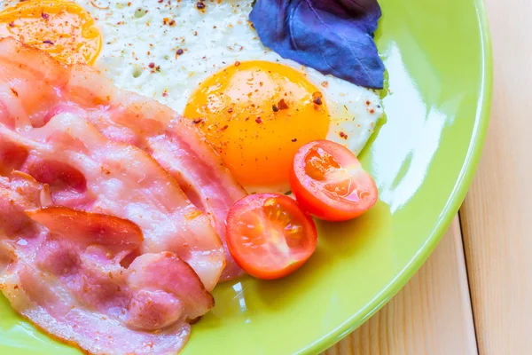 Fried eggs with bacon close-up on a green plate — Stock Photo, Image