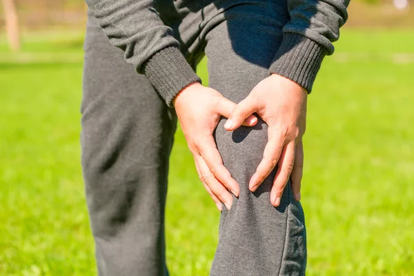 Manos masculinas apretado dolor de rodilla al aire libre — Foto de Stock