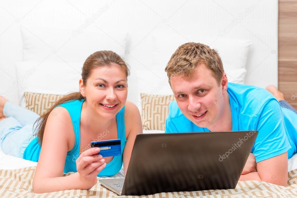 husband and wife with a credit card and a laptop on the bed in t