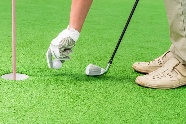 La mano di en in un guanto che mette una palla da golf vicino al foro — Foto Stock