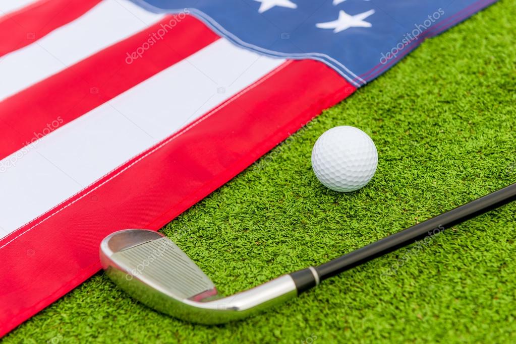putter and ball lie on the grass near to a flag of America