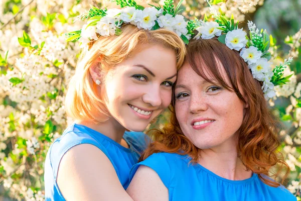 Duas namoradas com grinaldas na cabeça perto da che florescente — Fotografia de Stock