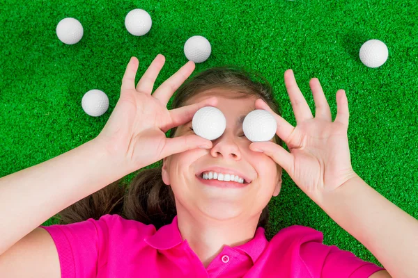 Girl with golf balls before his eyes laughing lying on the grass — Stock Photo, Image