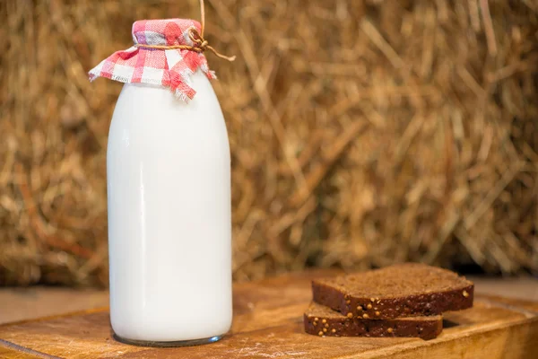 Bottle of milk and a piece of rye bread on a straw background — Stock Photo, Image