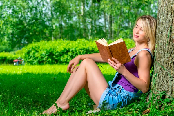 Attractive young woman reading a novel in the park sitting near — Stock Photo, Image