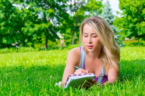 Attraktive junge Frau macht sich Notizen in einem Notizbuch, das auf dem g liegt — Stockfoto