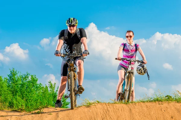 Een paar jonge fietsers op de heuvel tegen de hemel — Stockfoto