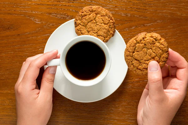 Manos sosteniendo una taza de café y galletas vista superior — Foto de Stock