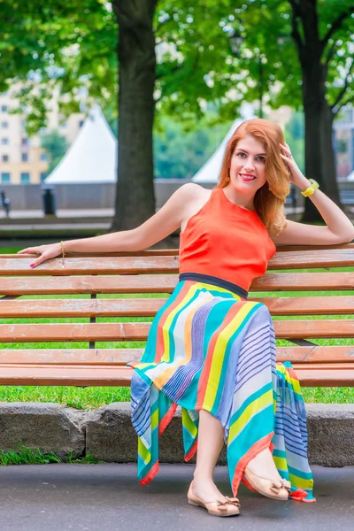 Vrouw in een helder oranje jurk op een bankje — Stockfoto