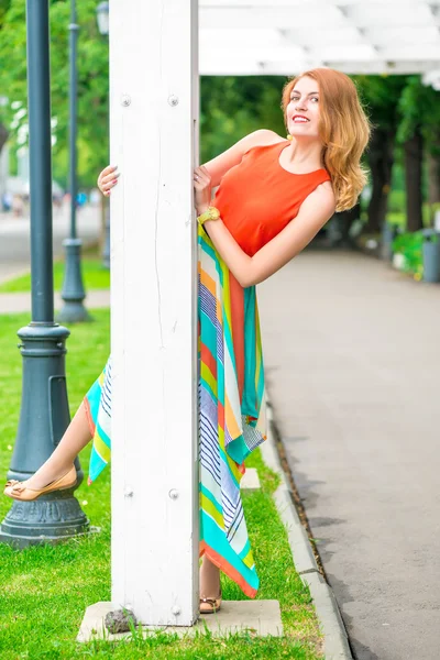 Веселая девушка смотрит из-за колонны беседки в парке — стоковое фото
