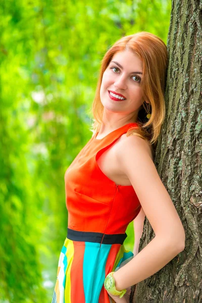 Resting beautiful girl at a tree trunk in the park — Stock Photo, Image