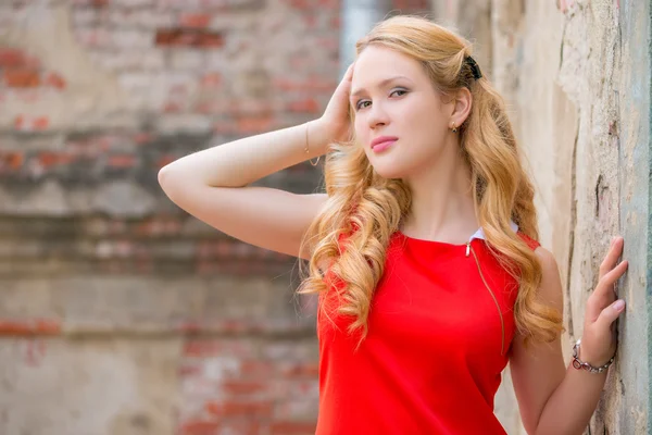 Schöne Blondine mit lockigem Haar posiert in der Nähe der Mauer — Stockfoto