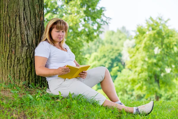 Mature woman of 50 years old reading a book on the lawn in the p — Stock Photo, Image