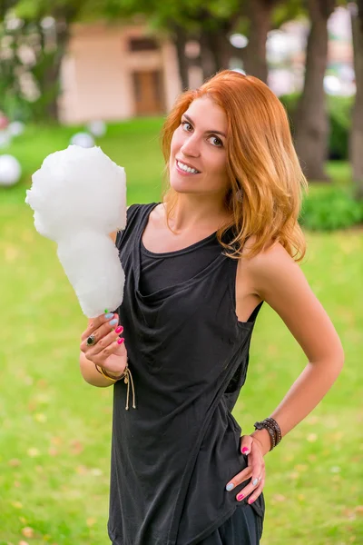 Sonriente chica en un parque es la celebración de un algodón de azúcar — Foto de Stock