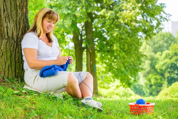 Horizontal portrait of a mature woman on a green lawn with knitt — Stock Photo, Image