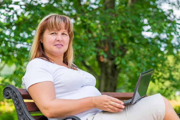Retrato de uma mulher em um banco no parque com um laptop — Fotografia de Stock
