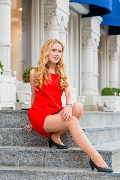 Girl in red dress with beautiful curls sitting on the steps — Stockfoto