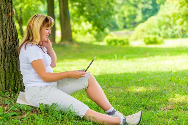 Mulher madura feliz no parque com um laptop — Fotografia de Stock