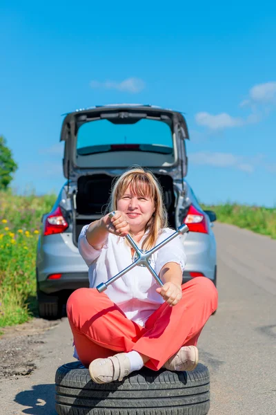 Retrato de uma mulher sentada com uma chave na roda — Fotografia de Stock