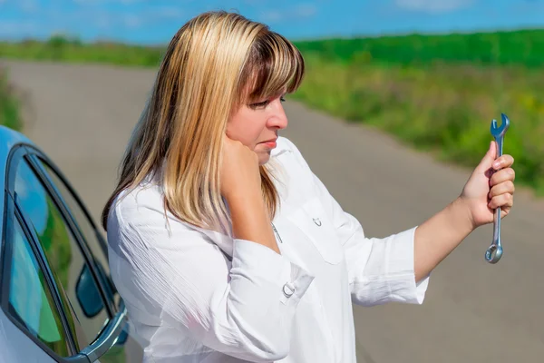 Bewildered female driver is looking at spanner — Stock Photo, Image