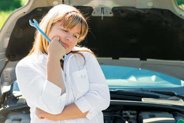 Mulher triste com uma chave inglesa perto do capô aberto de um carro — Fotografia de Stock