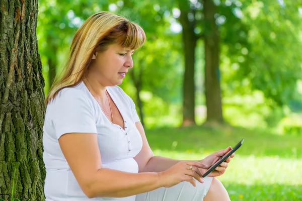 50 year old woman with a tablet in the summer park — Stock Photo, Image