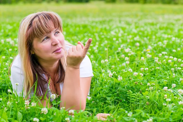 Mature woman on a green meadow showing a finger in the direction — Stock Photo, Image