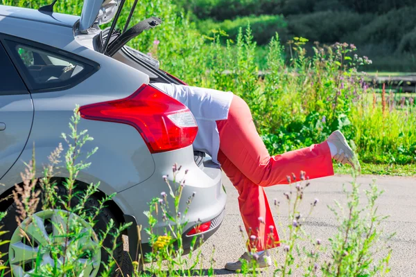 Women's legs sticking out of the trunk of the car on the road — Stock Photo, Image