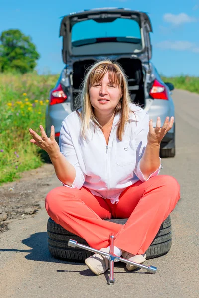 Annoyed woman sitting on the bursting of the wheel and waiting f — Stock Photo, Image