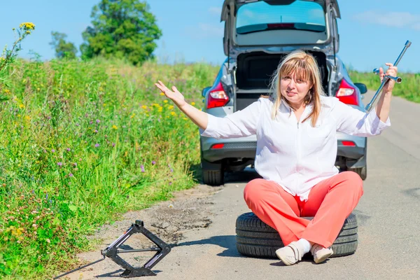 壊れた車に近いホイールに座って怒っている女性ドライバー — ストック写真