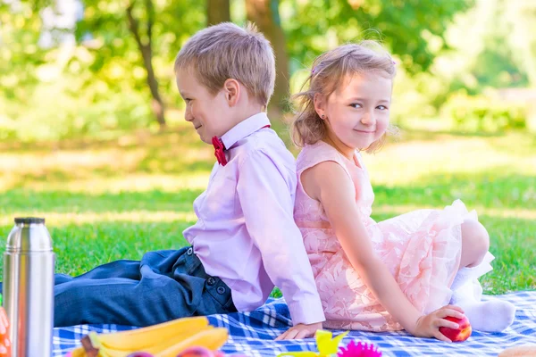 Jongen en een meisje van 6 jaar op een picknick rug aan rug zitten — Stockfoto