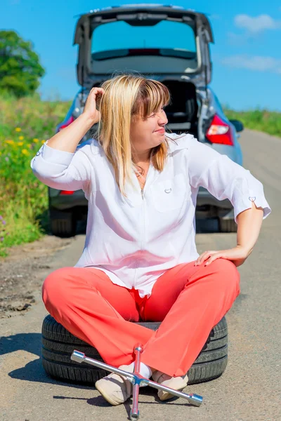 Mature female driver sitting in the spare wheel on a sunny day — Stock Photo, Image