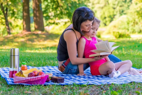 Mutter und Tochter lesen ein Buch auf dem Rasen im Park — Stockfoto