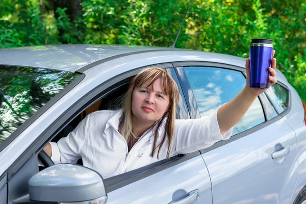 Mujer madura con una bebida mira por la ventana del coche mientras conduce —  Fotos de Stock