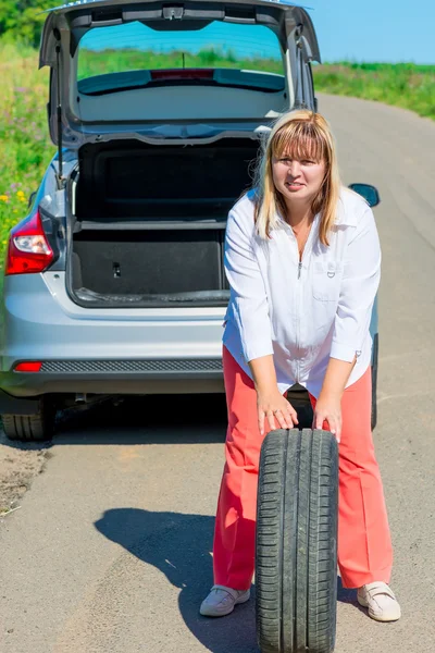 Mature woman posing with a spare wheel near the car — Stock Photo, Image