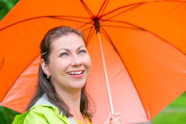 Laughing pretty girl with an orange umbrella walking in the rain — Stock Photo, Image