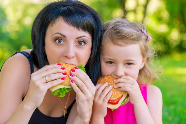 Portret matki z córką w parku z hamburgery — Zdjęcie stockowe